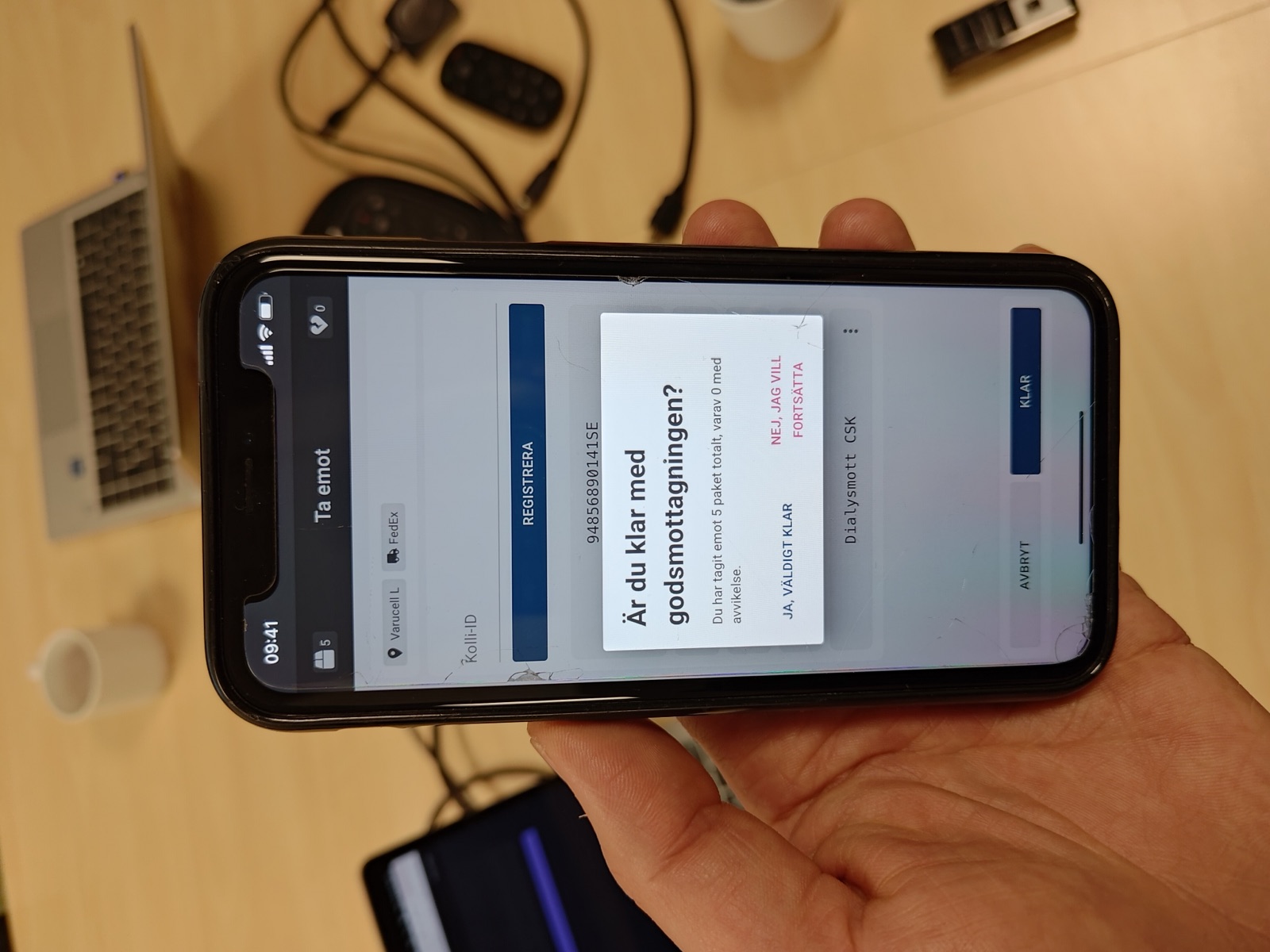 En hand håller en mobil med prototypen öppen i vyn Ta emot, där en dialog frågar om godsmottagningen är klar